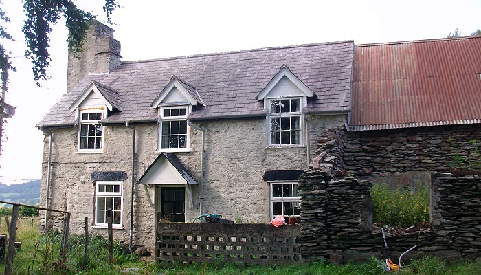 Two storey slate house with 3 dormers and attached barn with corrugated metal roof.