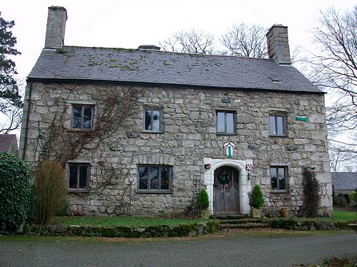 Large stone house with slate roof and chimney at each gable.